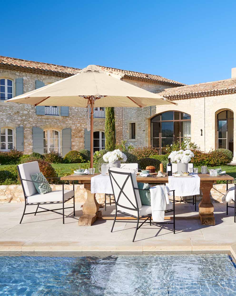 Conjunto de muebles de jardín con mesa de madera y sombrilla beige junto a la piscina en estilo rústico