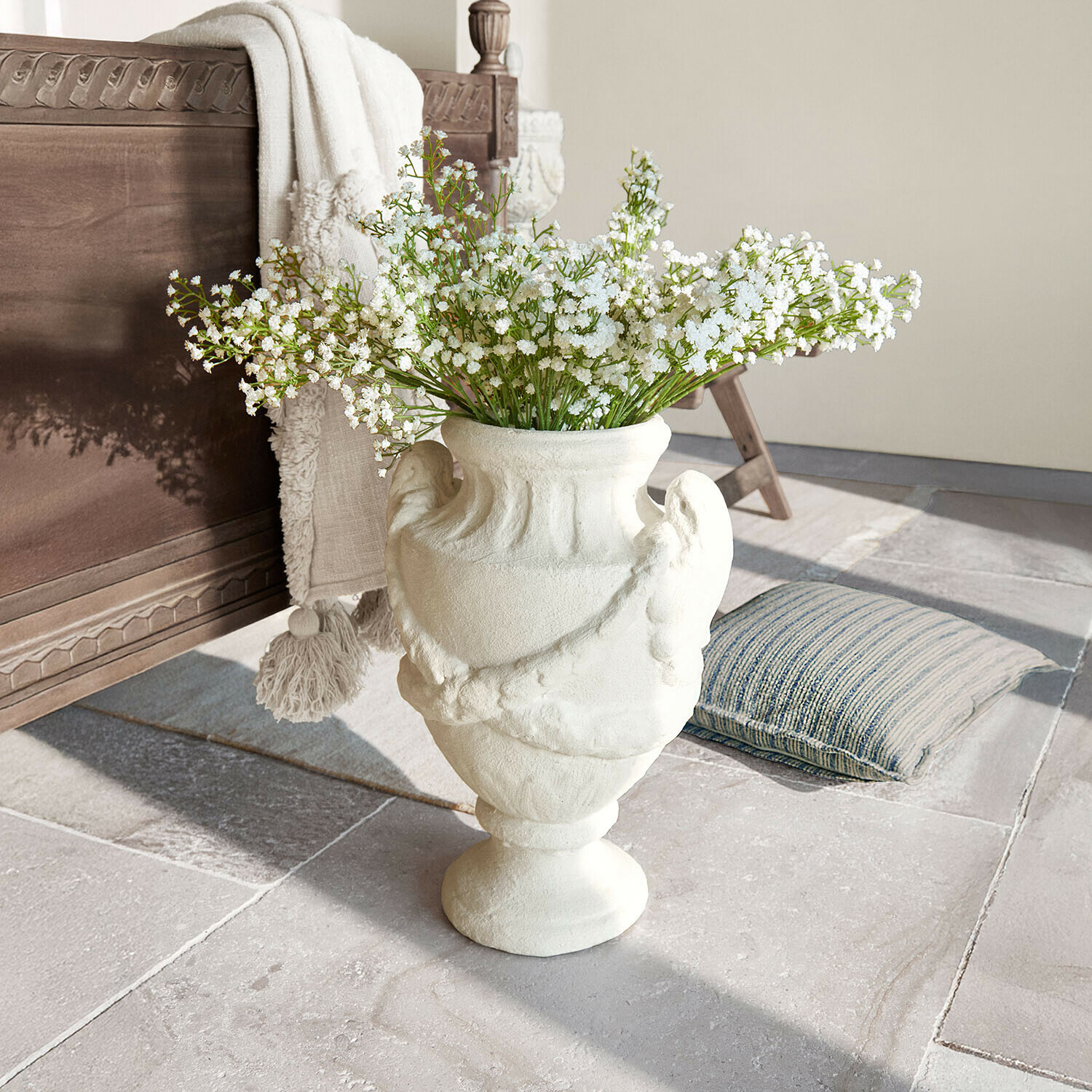 Jarrón de cerámica blanca con diseño decorativo y flores blancas sobre suelo de piedra