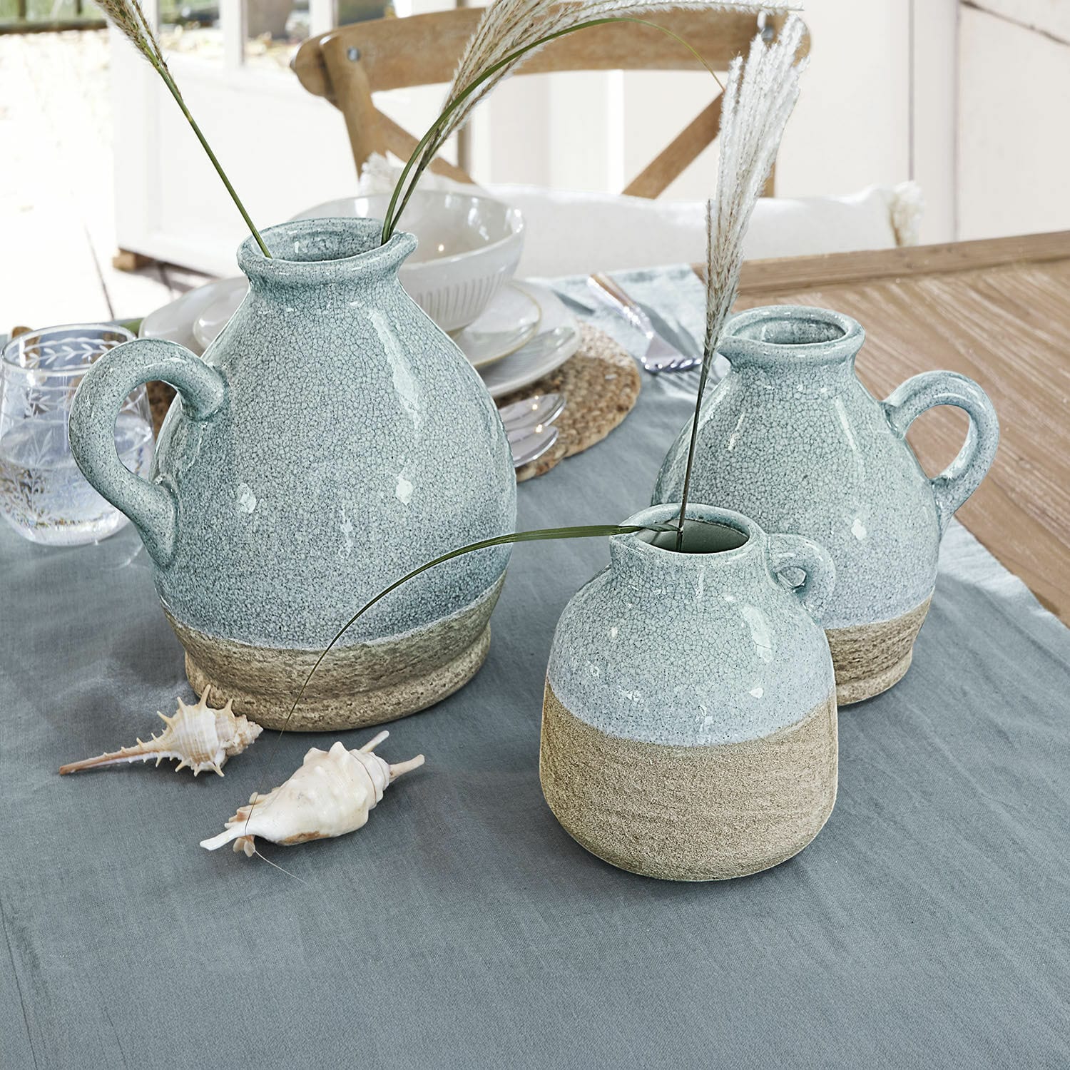 Set de 3 jarrones Lezíria Conjunto de tres jarrones de cerámica azul y beige sobre mesa con decoración de conchas
