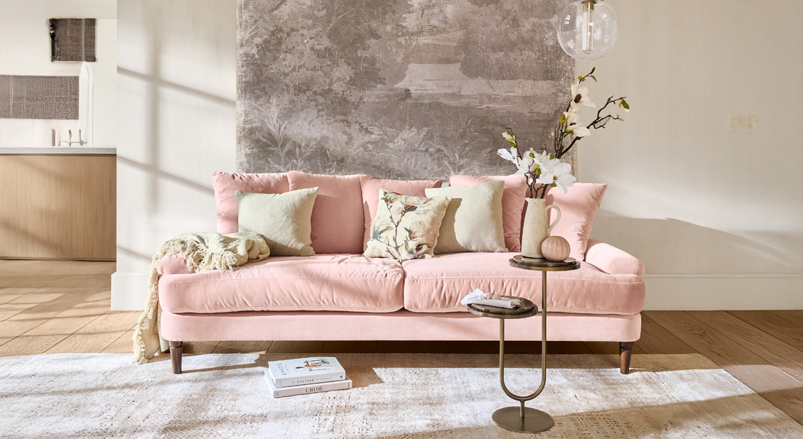 Sofá rosa de terciopelo con cojines y mesa auxiliar en salón moderno y luminoso