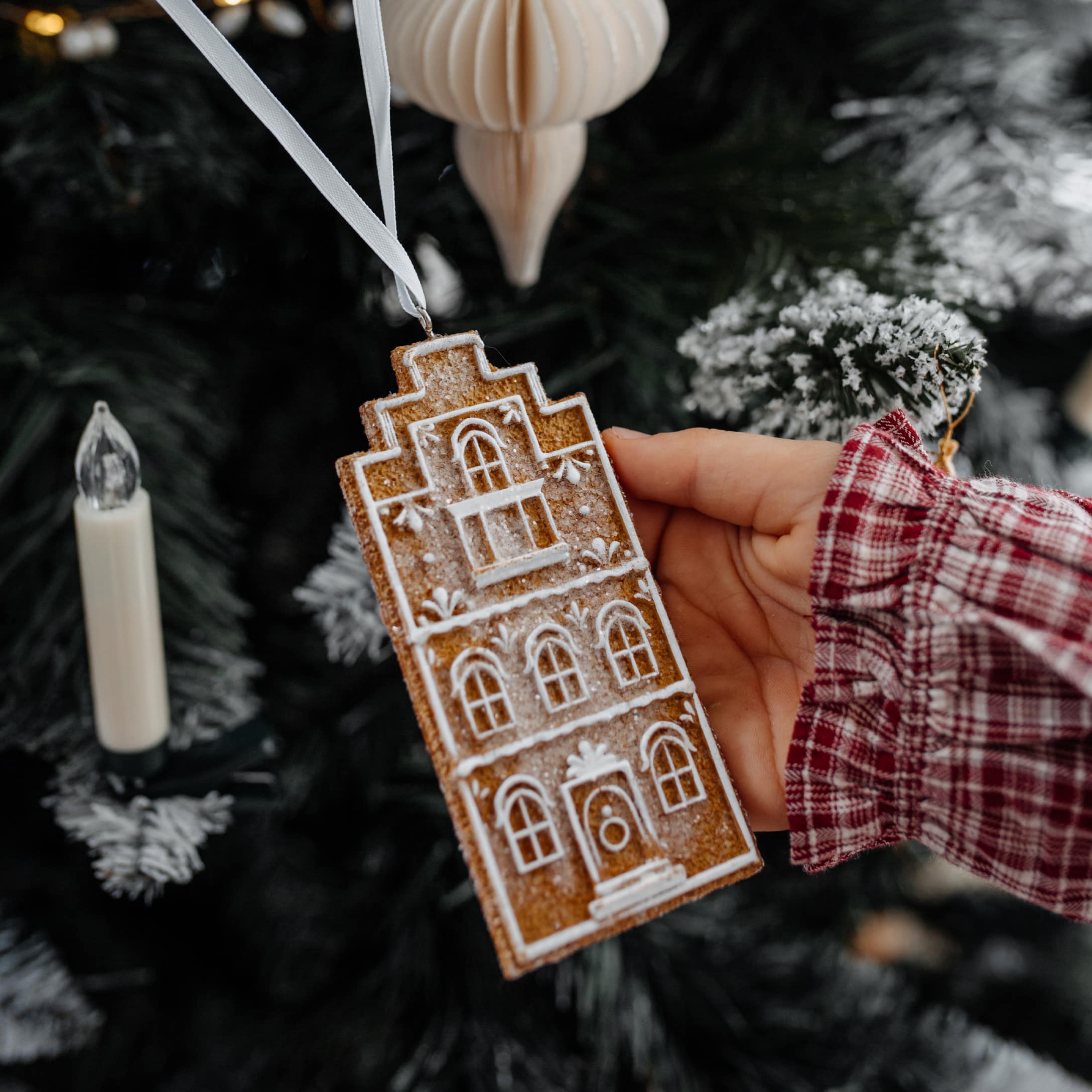 Adorno navideño en forma de casa de jengibre con diseño blanco, colgado de una cinta blanca