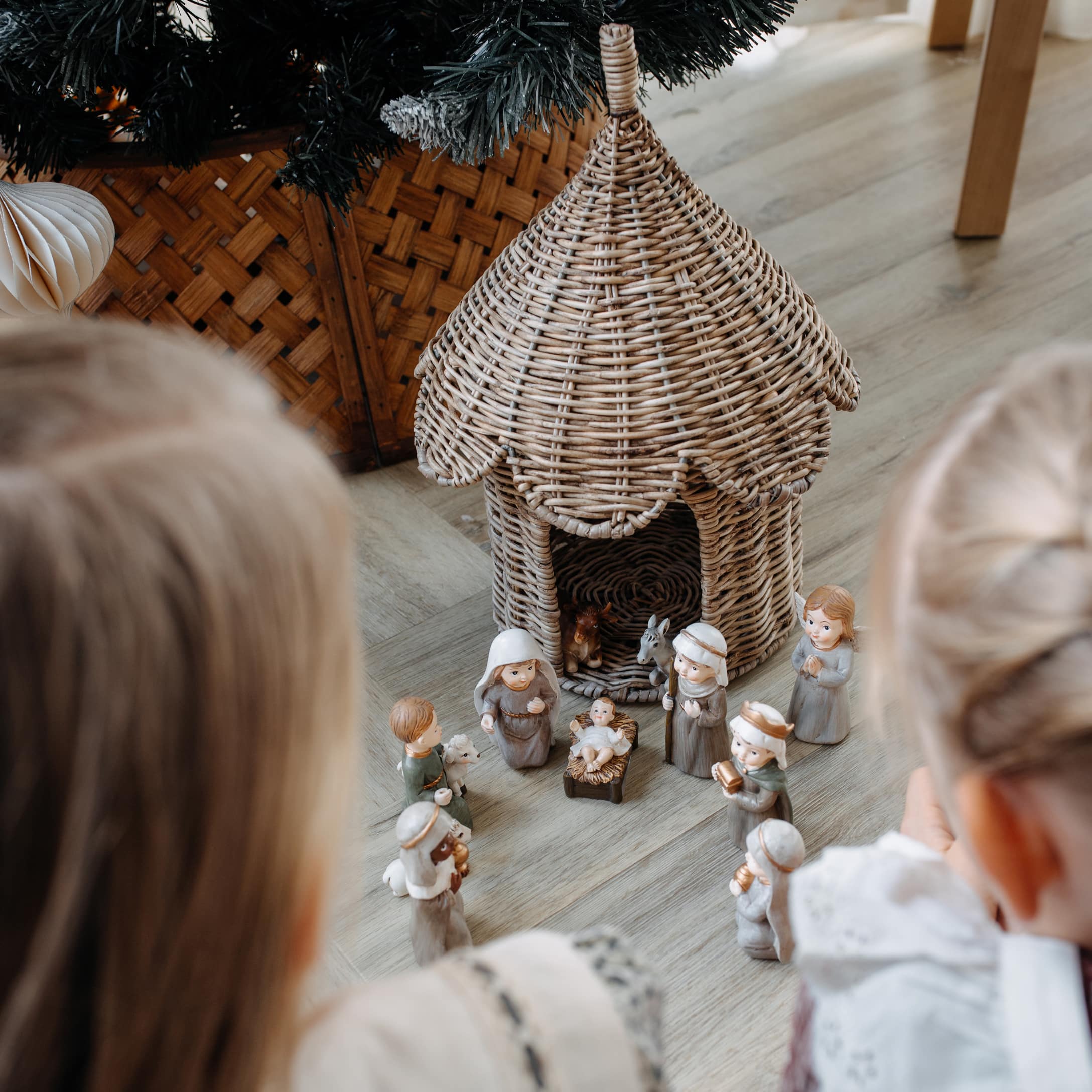Niños observan un belén navideño con figuras de cerámica y casa de mimbre en el suelo