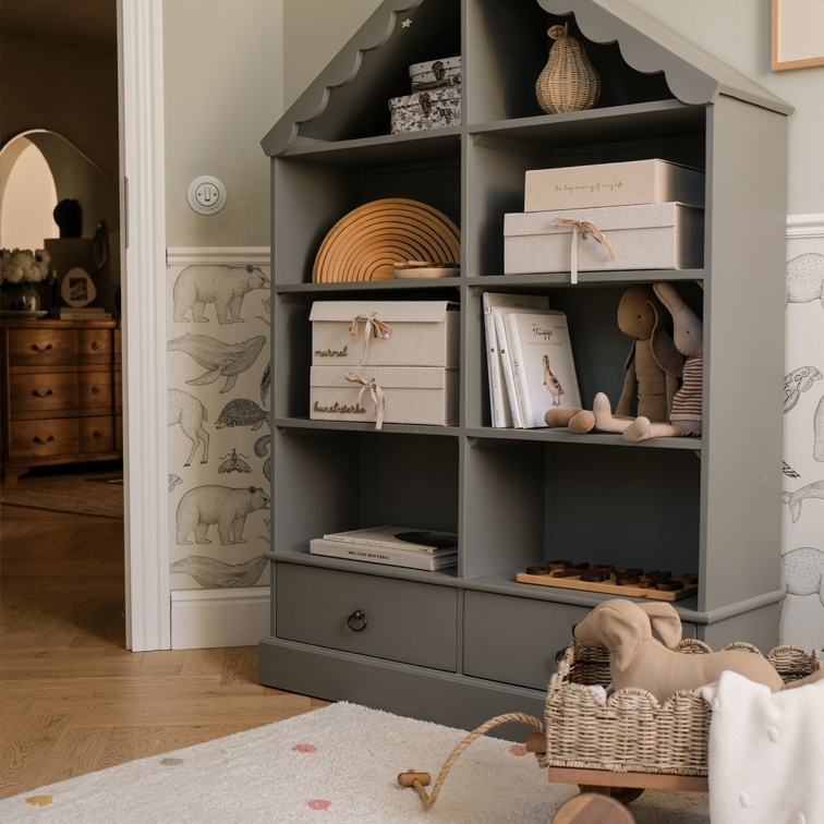 Estantería gris de madera con forma de casa con cajas, libros y peluches en habitación infantil