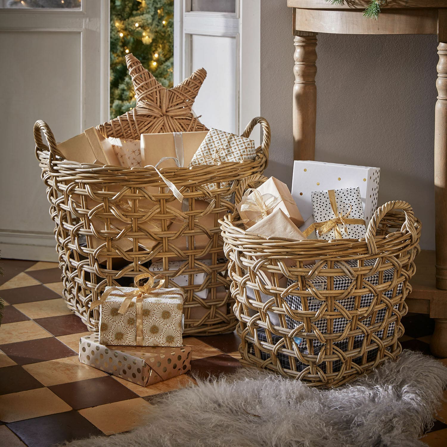 Set de 2 cestas Qivoran Dos cestas de mimbre natural con regalos y decoraciones navideñas sobre suelo de baldosas.