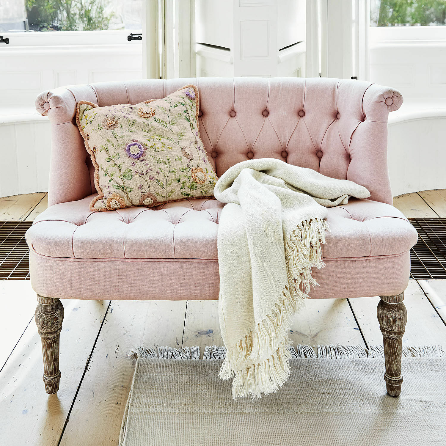 Sofá Weralin Sofá tapizado rosa con patas de madera, cojín decorativo y manta crema sobre el asiento