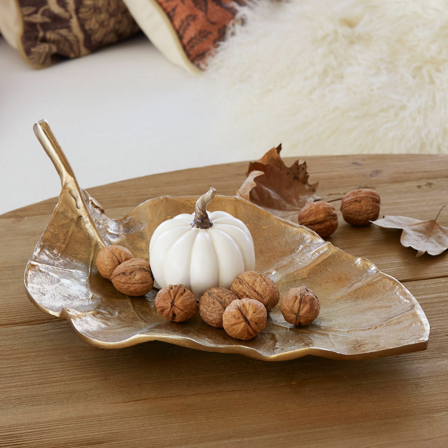 Bandeja dorada en forma de hoja con calabaza blanca y nueces sobre mesa de madera