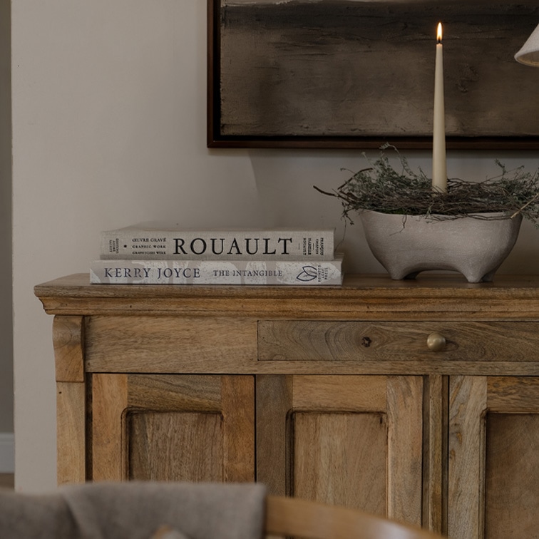 Aparador de madera con dos libros y vela encendida en cuenco de cerámica sobre mesa decorativa