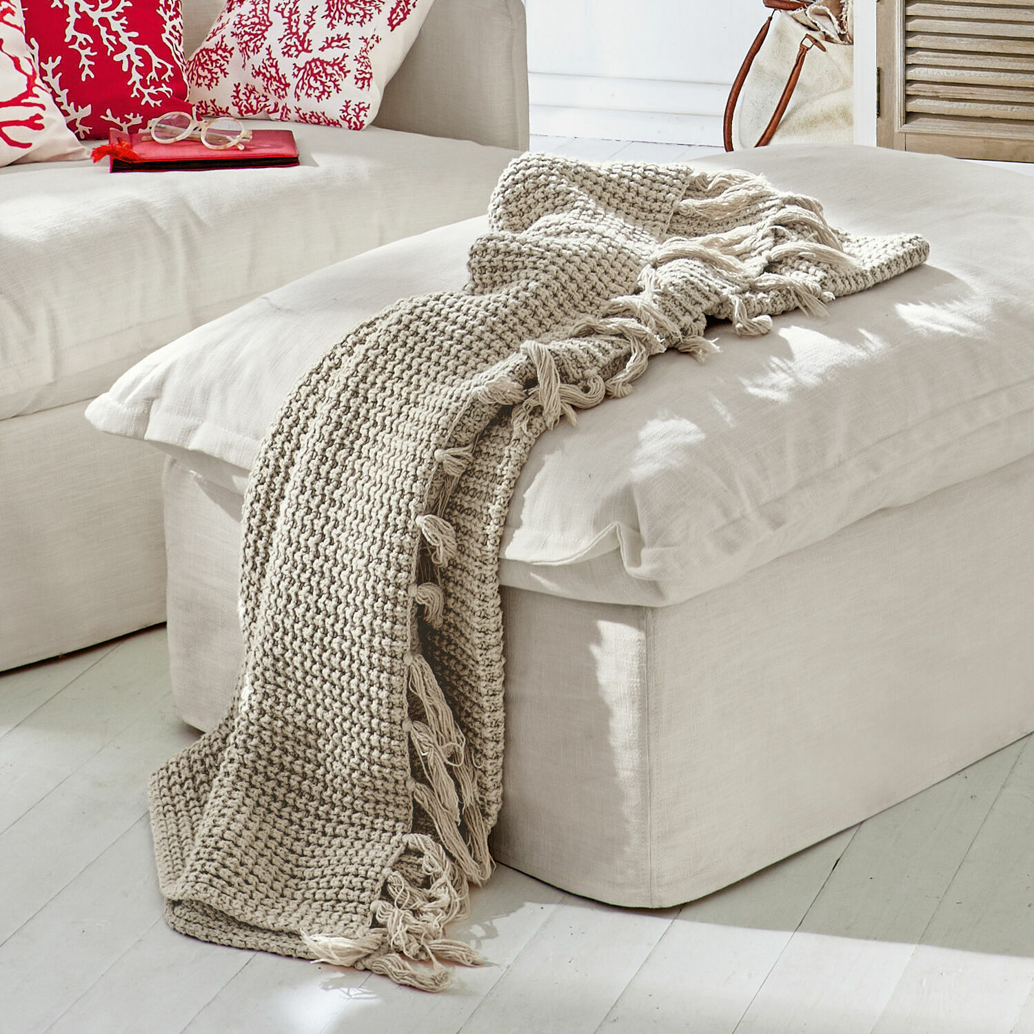 Plaid Kendall Manta beige tejida con flecos sobre un asiento claro en una sala moderna