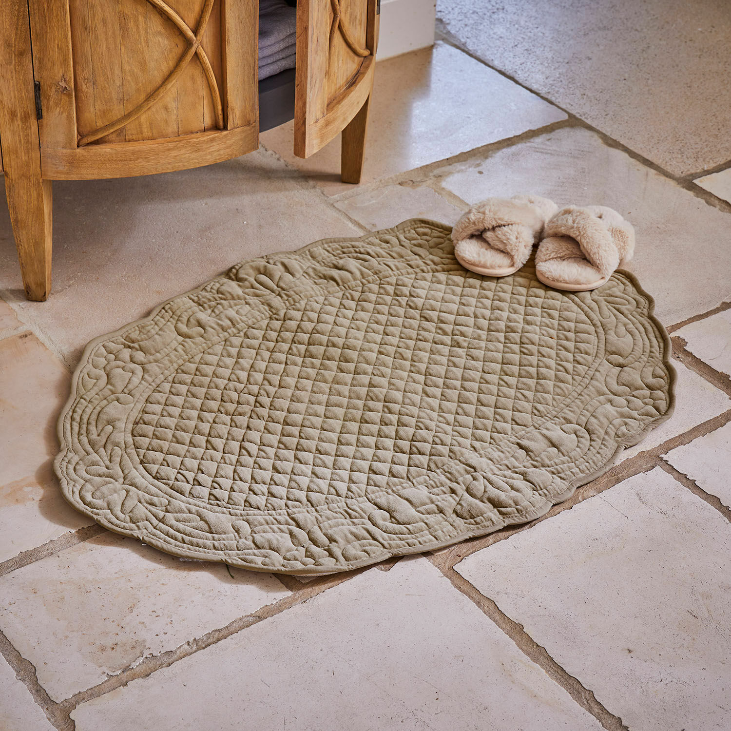 Alfombrilla de baño Courlevin Alfombrilla de baño ovalada acolchada en color oliva sobre suelo de piedra con zapatillas beige