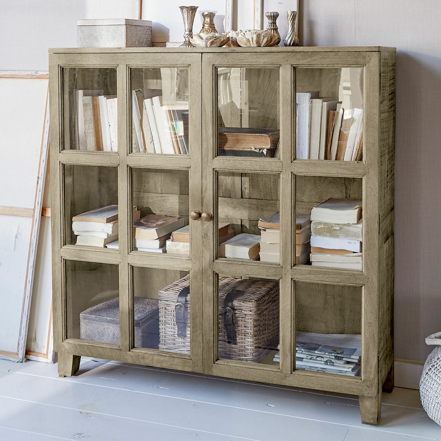 Cómoda Stoneham Vitrina de madera beige con puertas de cristal, llena de libros y decoraciones, mueble para salón