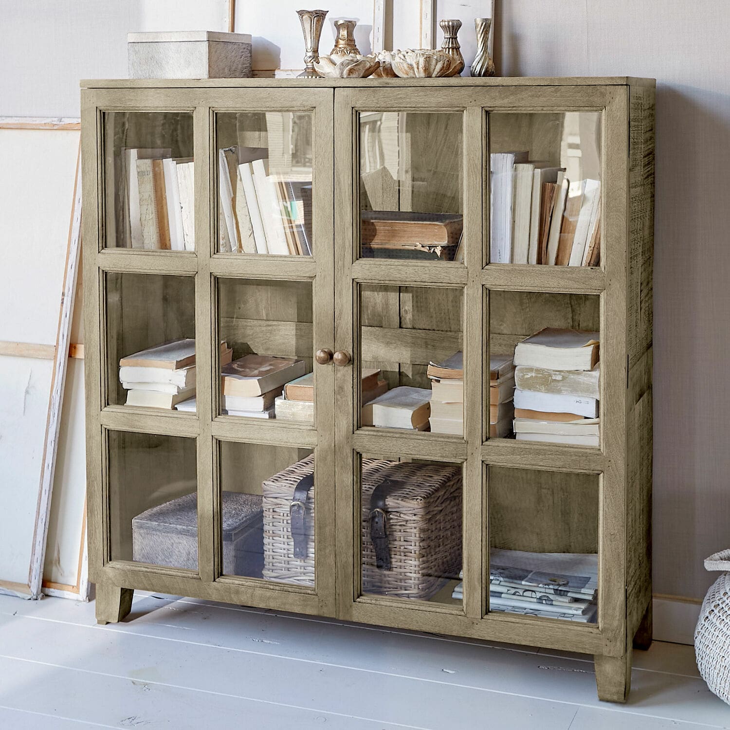 Cómoda Stoneham Vitrina de madera beige con puertas de cristal, llena de libros y decoraciones, mueble para salón