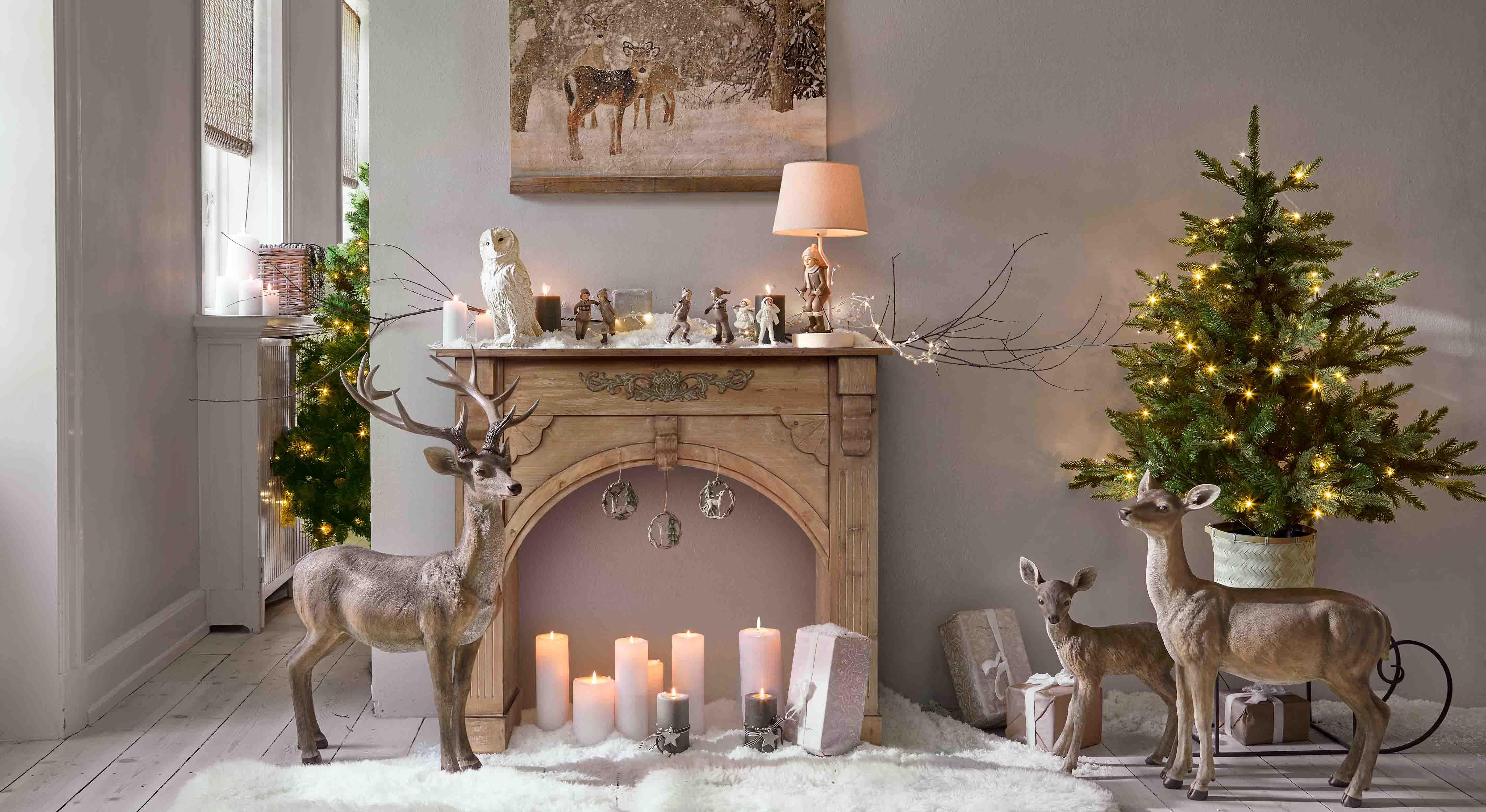 Decoración navideña con figuras de ciervos marrones, velas y árbol de Navidad verde con luces LED