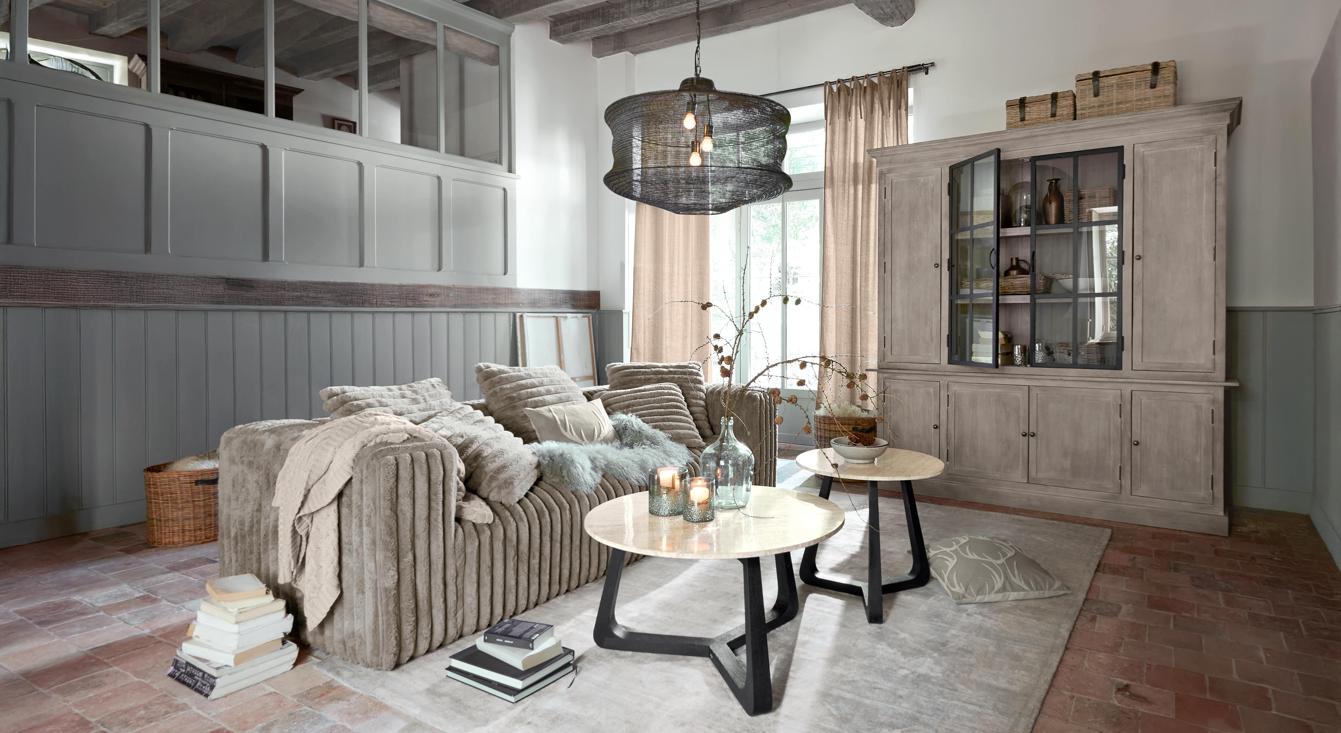 Salón acogedor con sofá beige de material suave y dos mesas de centro redondas con encimeras de mármol