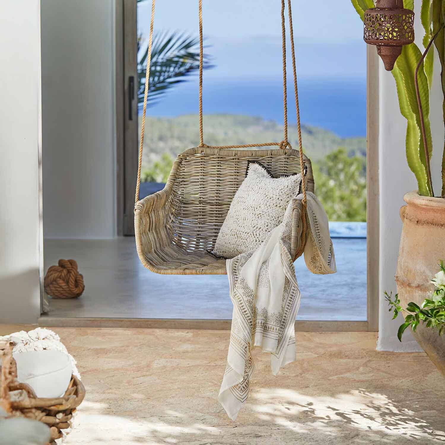 Columpio de ratán color natural con cojín blanco y chal decorativo en interior luminoso