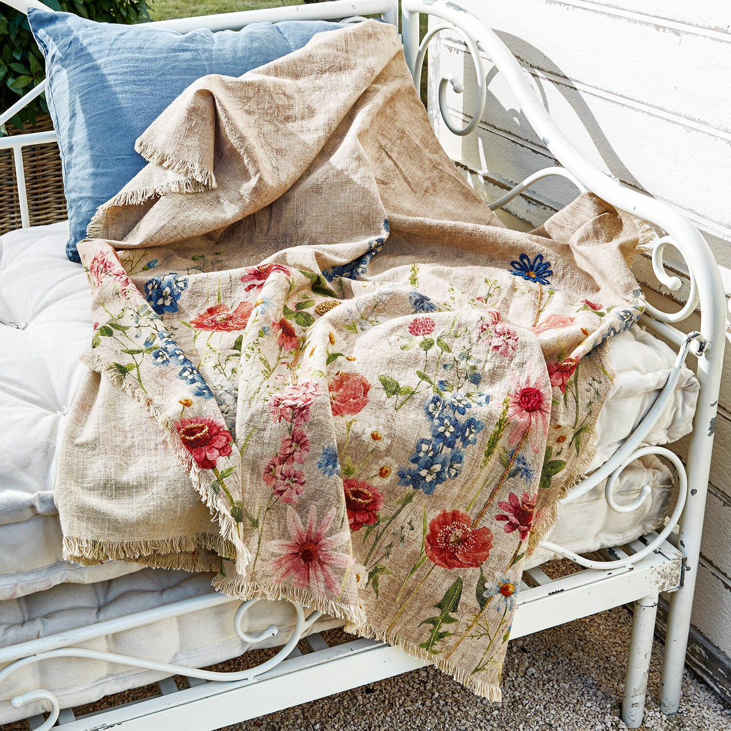 Estampado en lino Eleonoire Manta beige de lino con diseño floral colorido y flecos sobre banco metálico blanco
