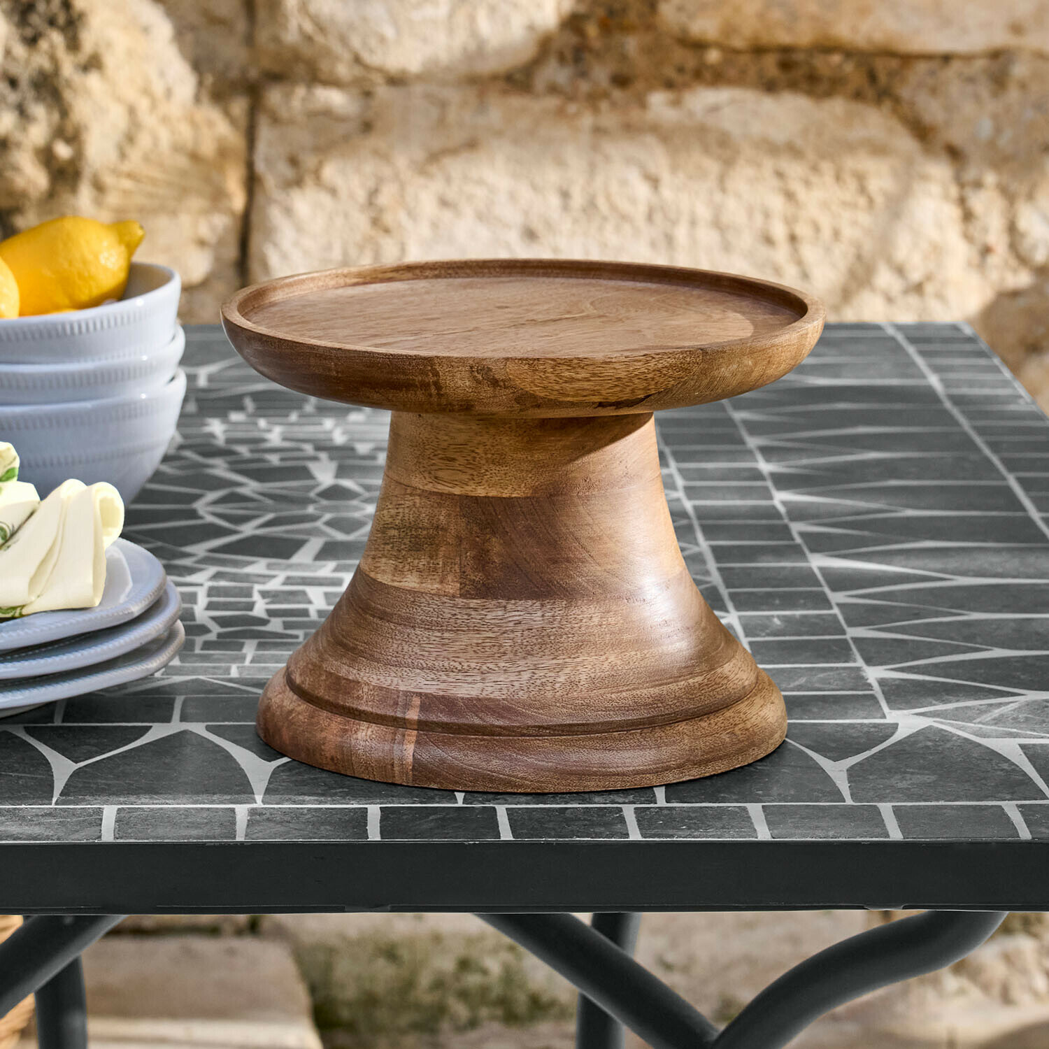 Plato de madera natural con base sobre mesa de mosaico, perfecto para servir pasteles y aperitivos