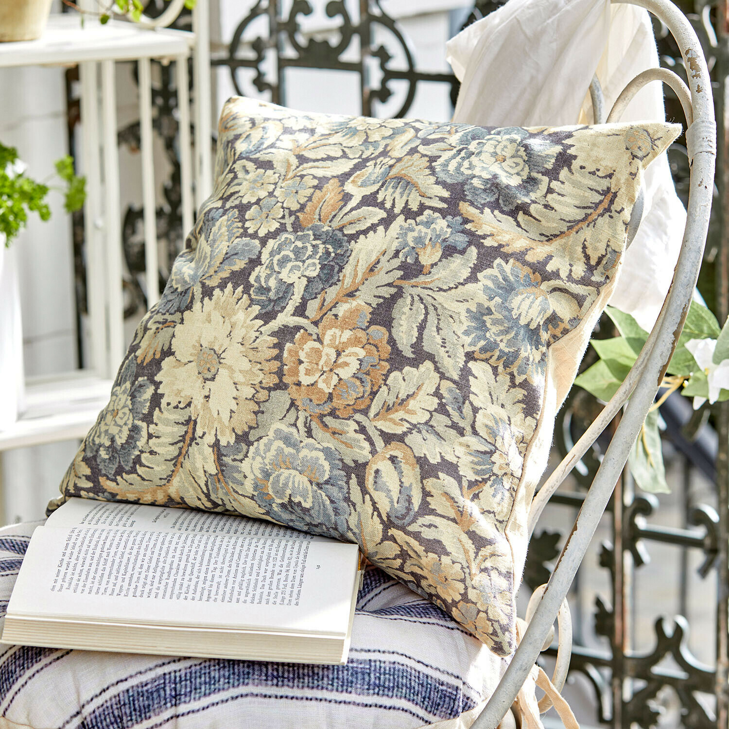 Funda de cojín Lumielle Cojín decorativo de tela con diseño floral en tonos beige y azul sobre silla metálica blanca