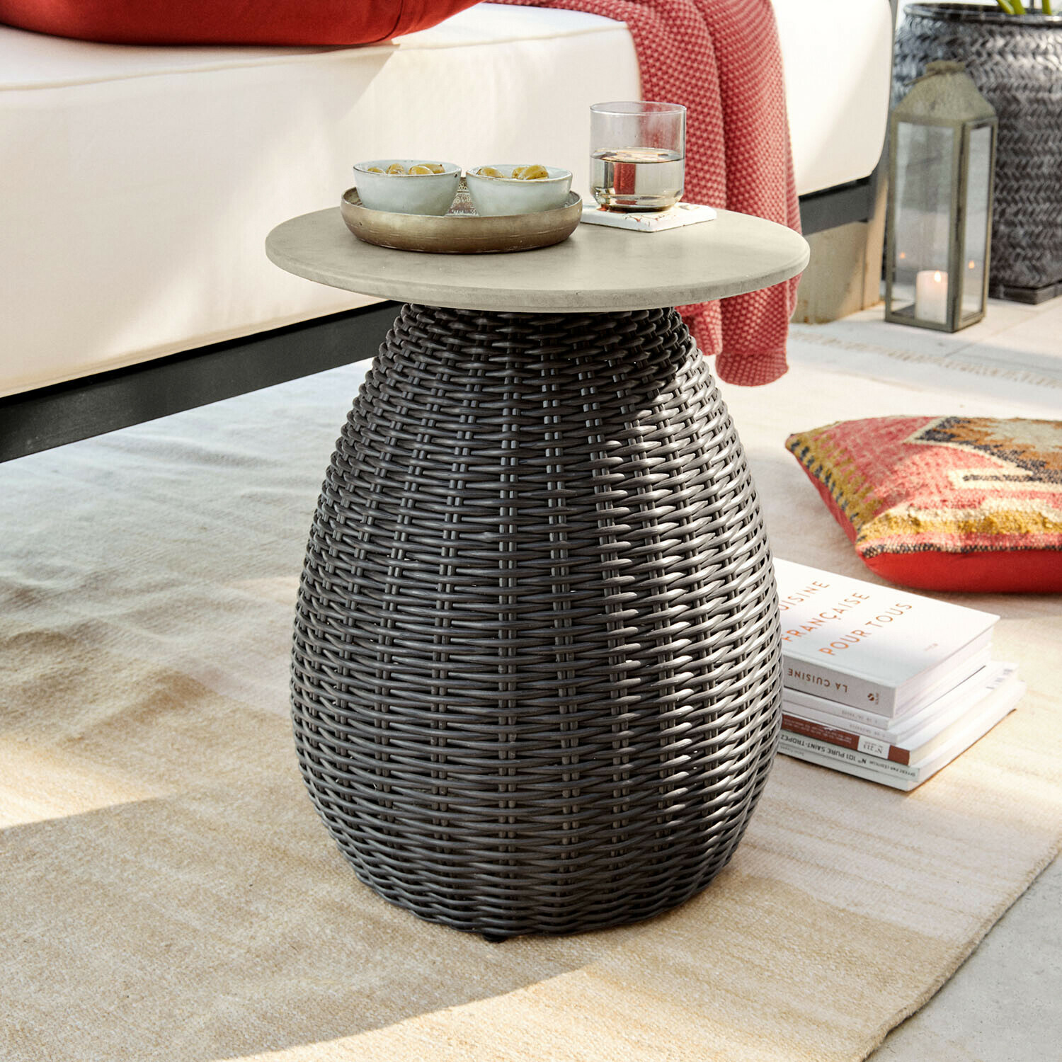Mesa auxiliar Tarevo Mesa auxiliar redonda con superficie gris y base de mimbre gris oscuro sobre alfombra en sala