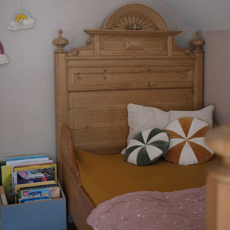 Cama de madera maciza con cabecero decorativo, cojines y libros en habitación infantil