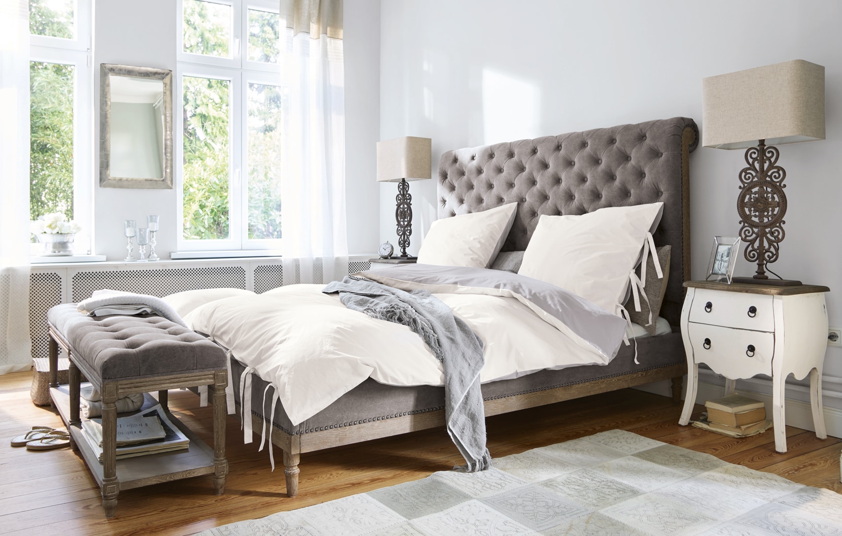 Dormitorio clásico con cama tapizada gris y ropa de cama blanca en interior luminoso