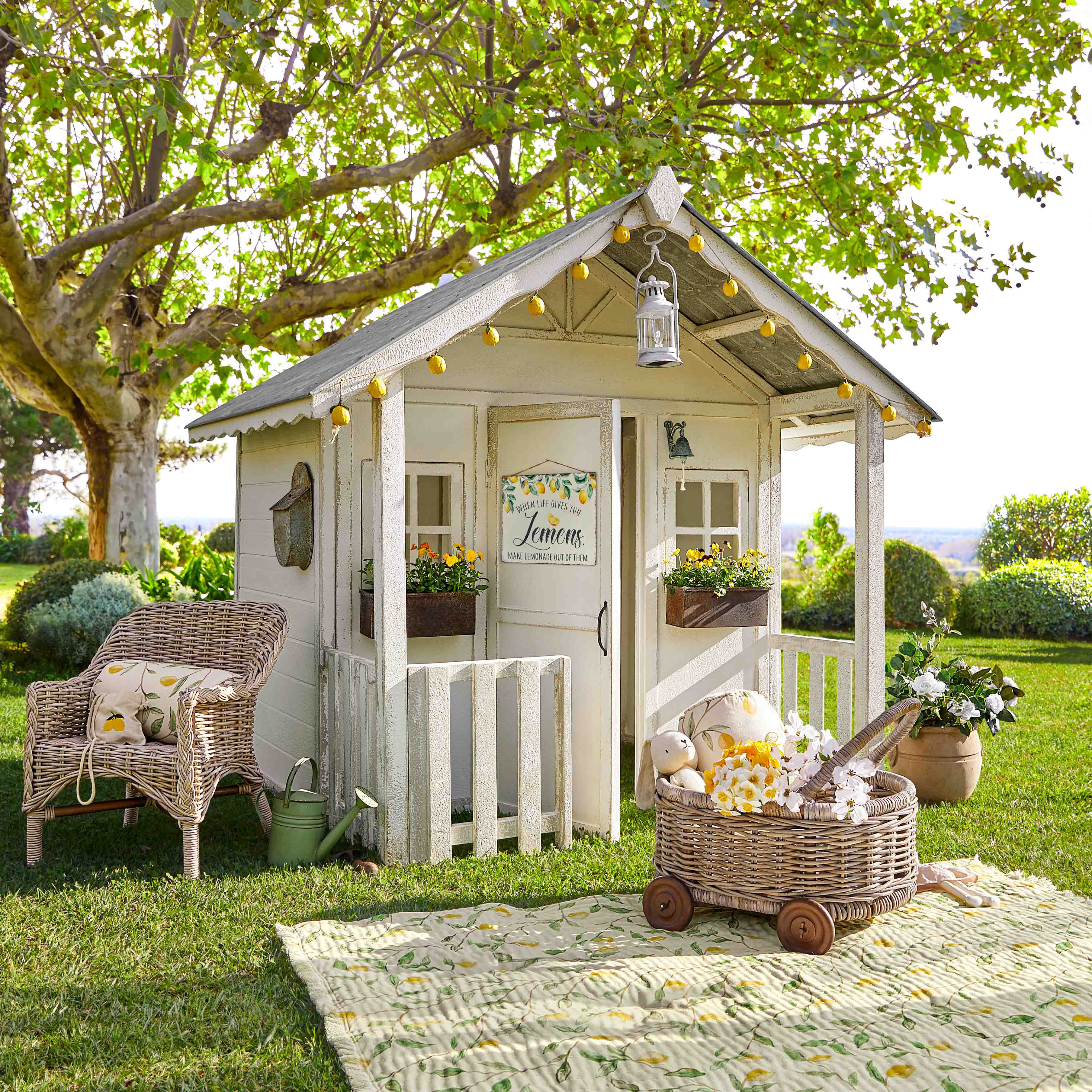 Casita de jardín de madera blanca con guirnalda de luces y flores sobre césped verde