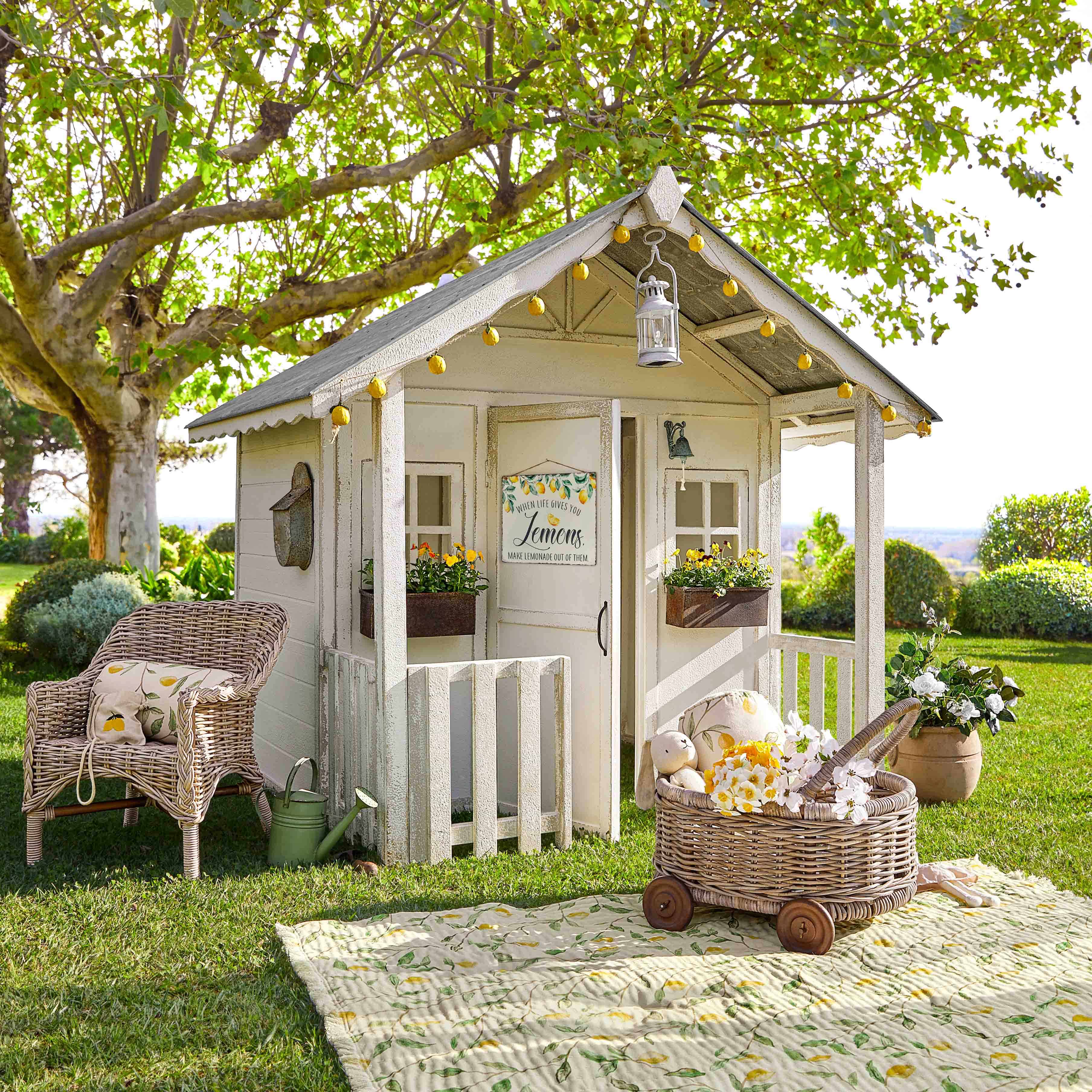Casita de jardín de madera blanca con guirnalda de luces y flores sobre césped verde