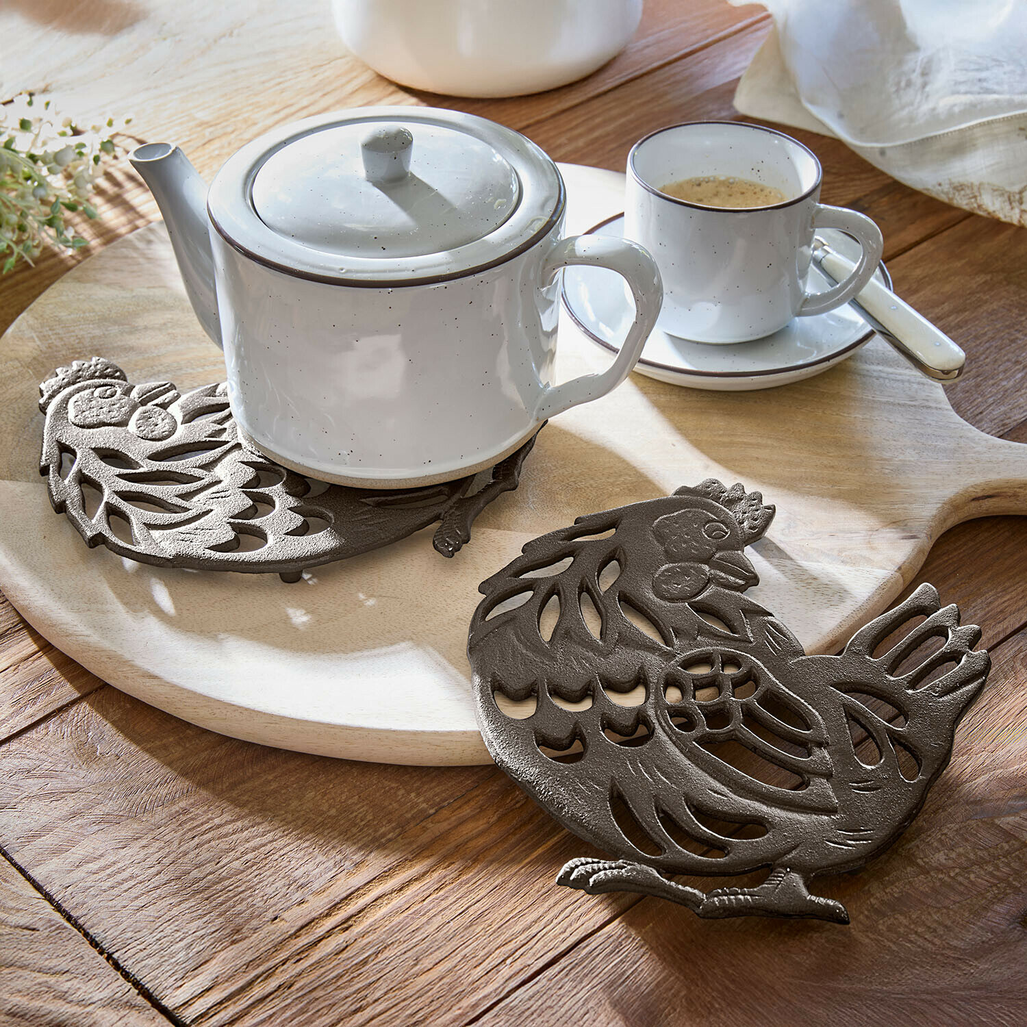 Set de 2 salvamanteles Chavéreau Salvamanteles de hierro fundido marrón con forma de gallina sobre mesa de madera con tetera y taza blanca
