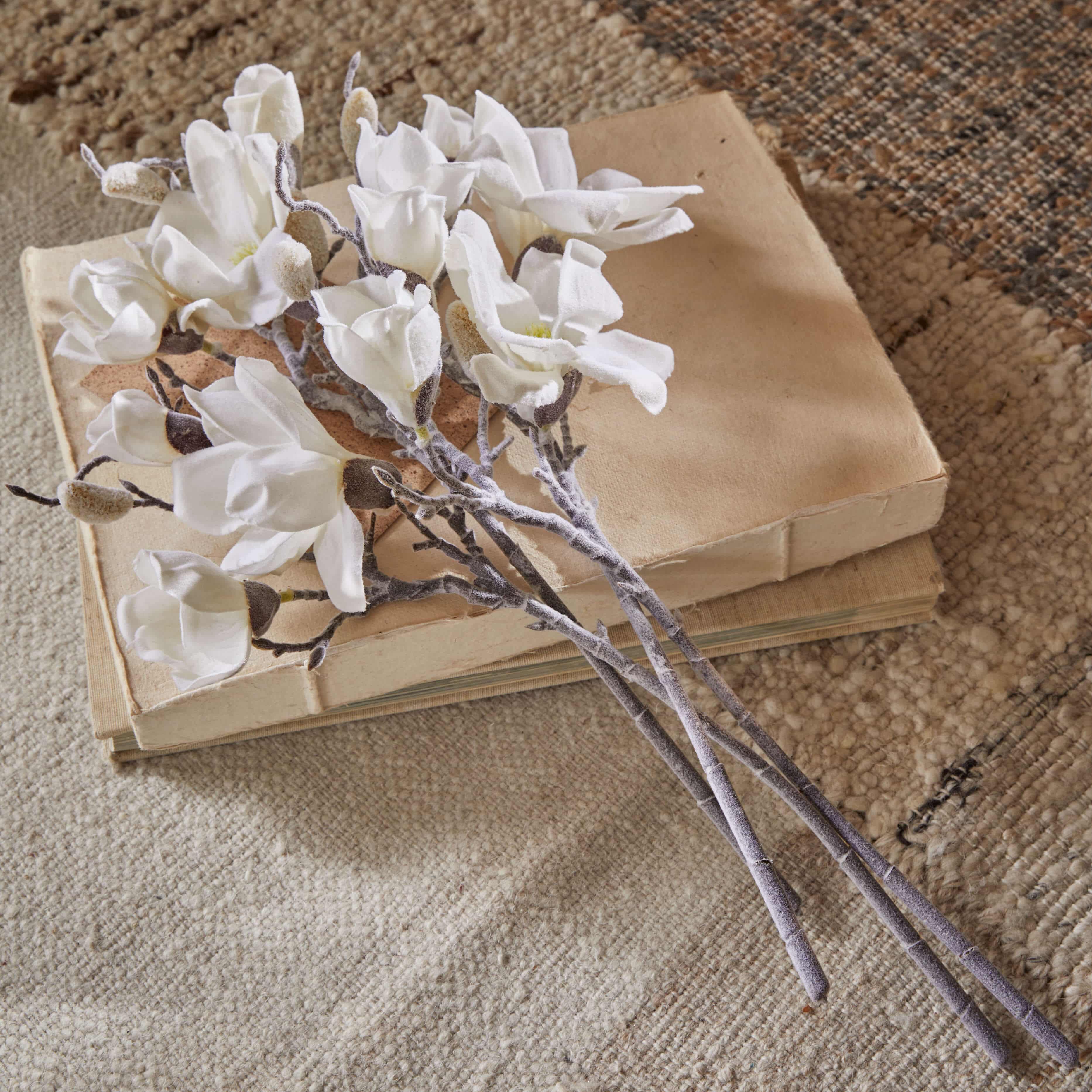 Ramo de flores de magnolia blancas de tela sobre libros antiguos beige en alfombra