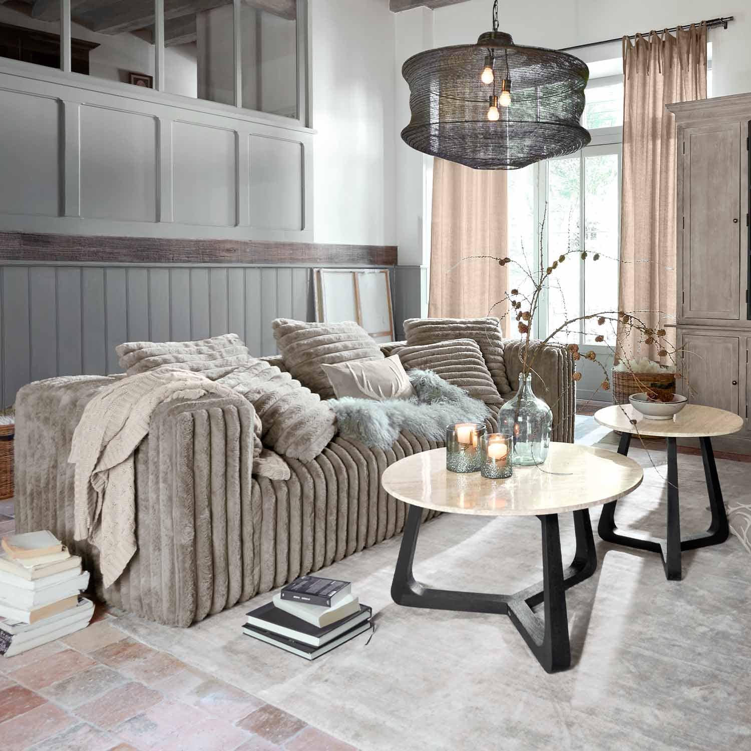 Sofá beige de material suave en salón moderno con dos mesas de centro redondas de madera y metal