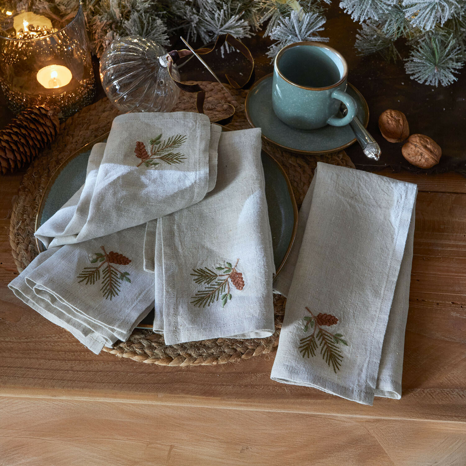 Set de 4 servilletas Arlida Servilletas de lino bordadas con piñas sobre mesa rústica con decoración navideña