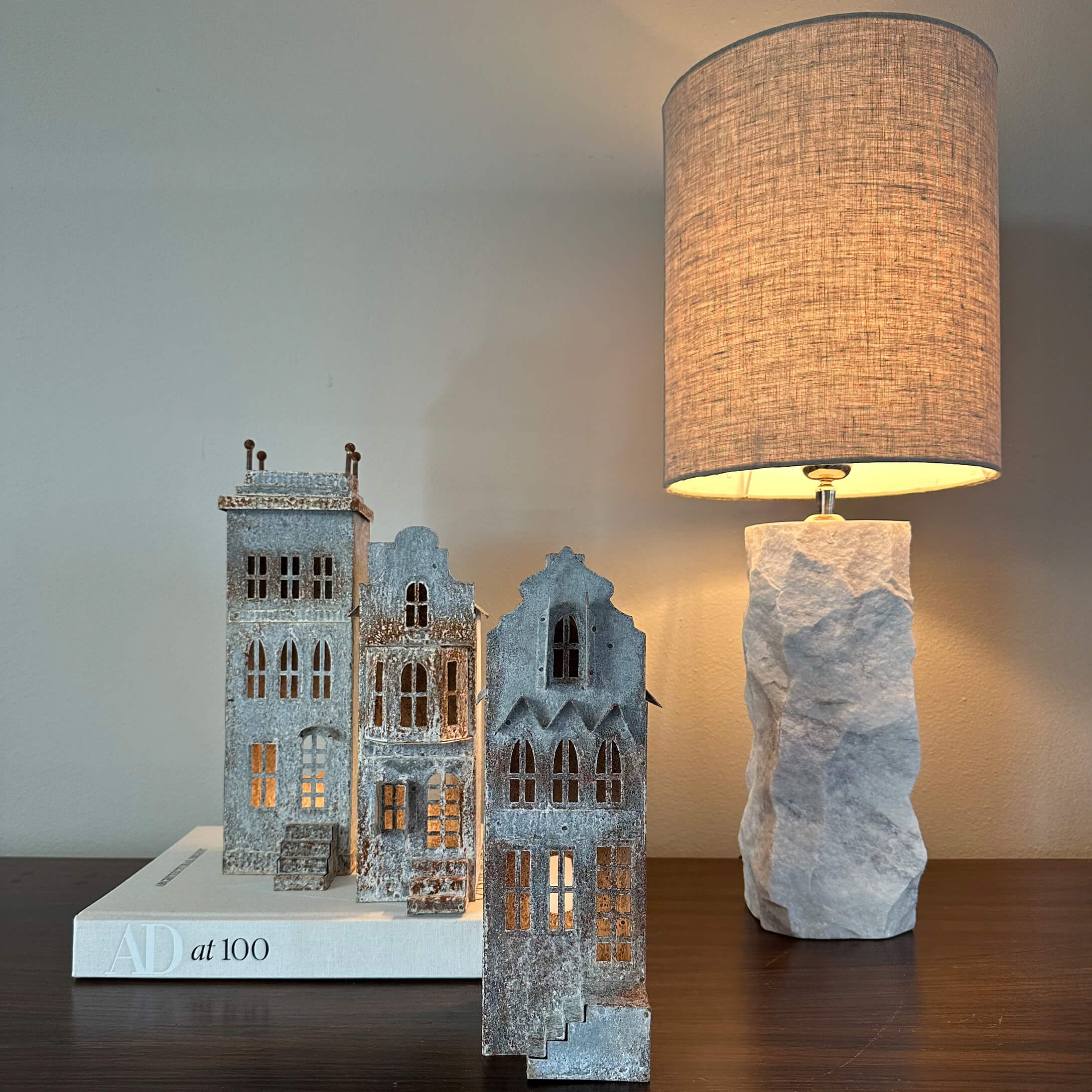 Casas decorativas de metal gris sobre libro blanco junto a lámpara con base de piedra