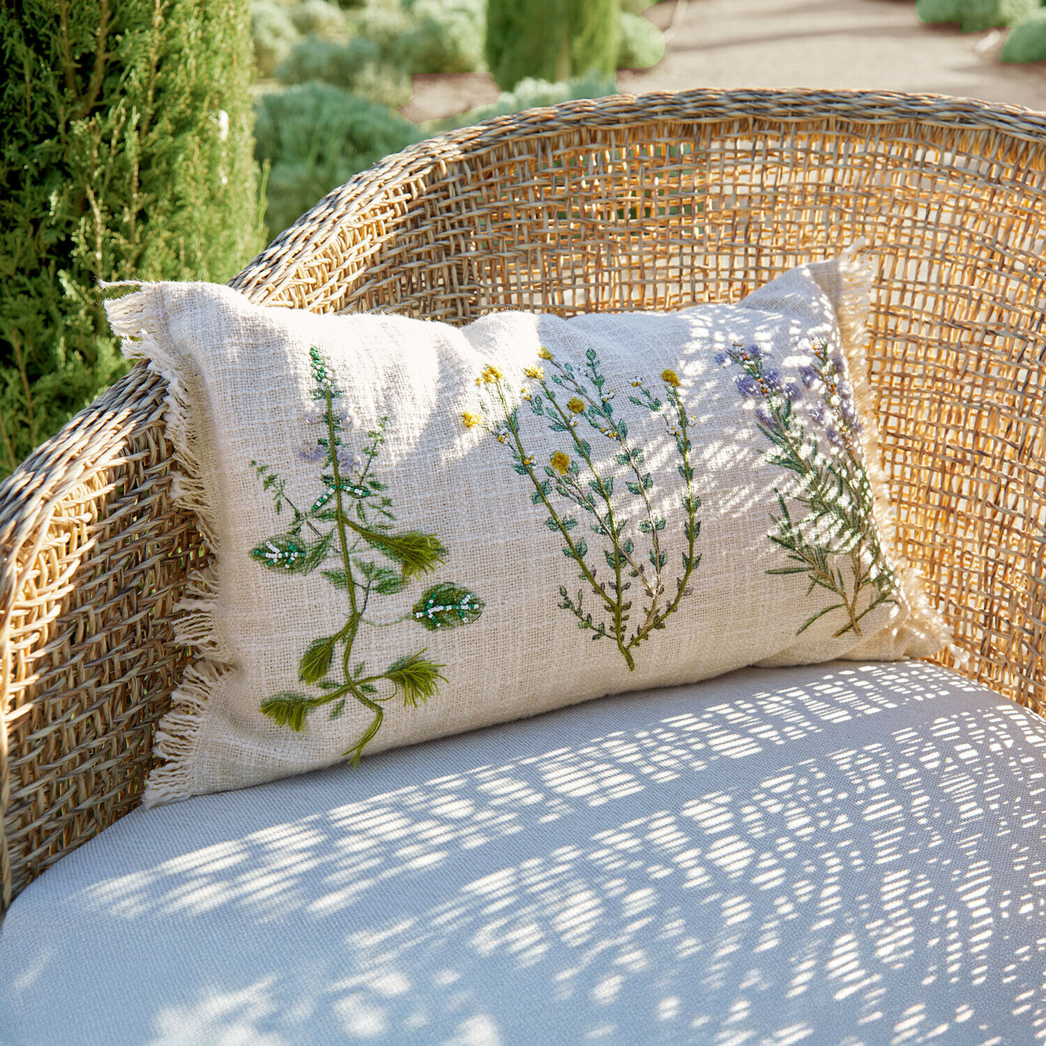 Funda de cojín Sélomiane Cojín de lino beige con bordado vegetal sobre sillón de mimbre, decoración de jardín