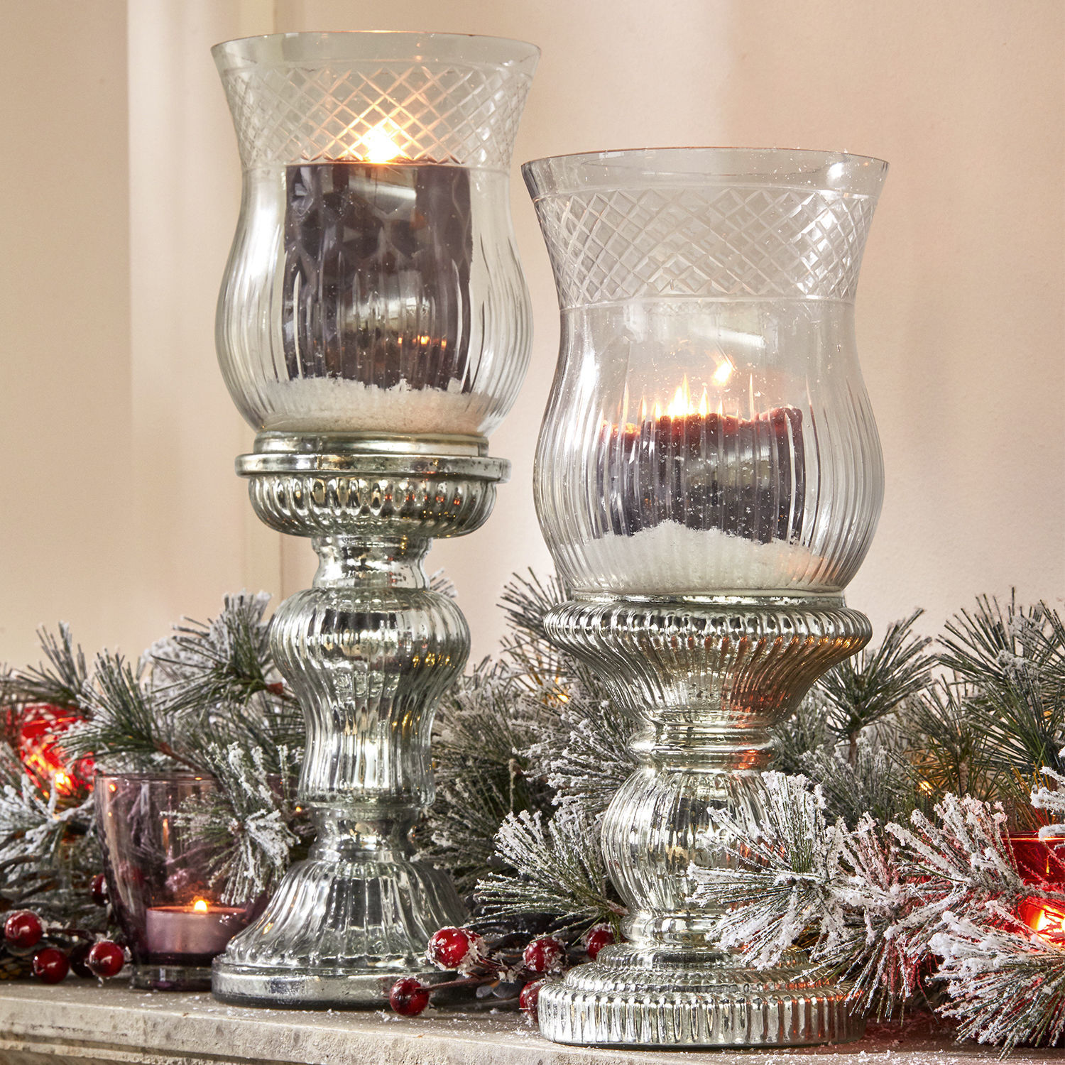Portavelas de vidrio con base metálica plateada y velas negras, decoración navideña con ramas y bayas rojas