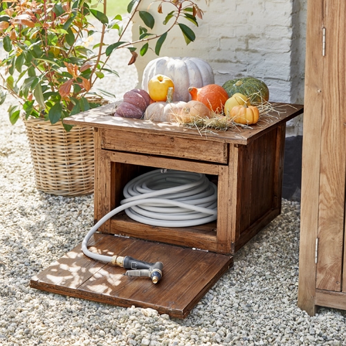Caja de jardín de madera con manguera blanca y calabazas decorativas sobre grava