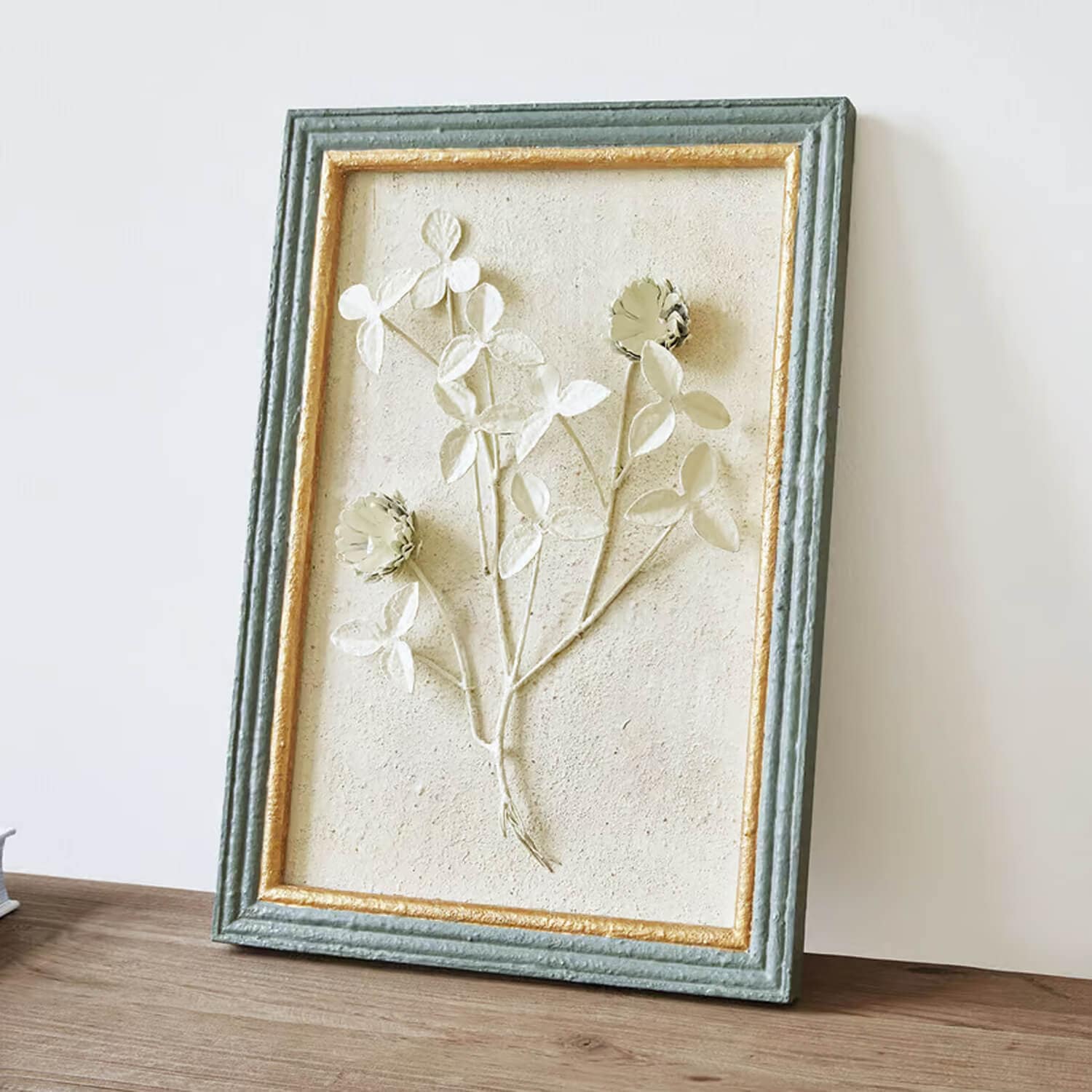 Relieve decorativo floral en marco texturizado verde y dorado sobre fondo beige claro