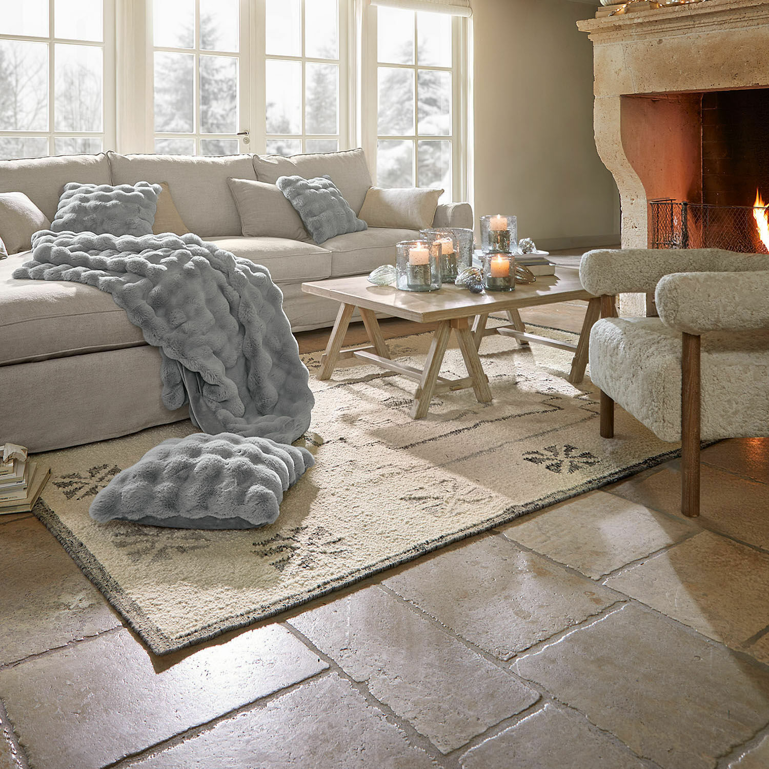 Sala acogedora con sofá beige, manta y cojín gris de felpa, chimenea y mesa de madera