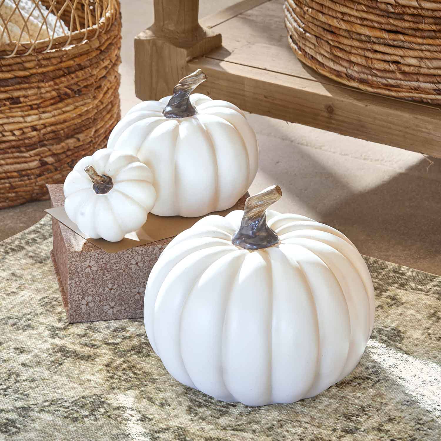 Calabazas decorativas blancas de plástico con tallos marrones sobre alfombra y mesa de madera