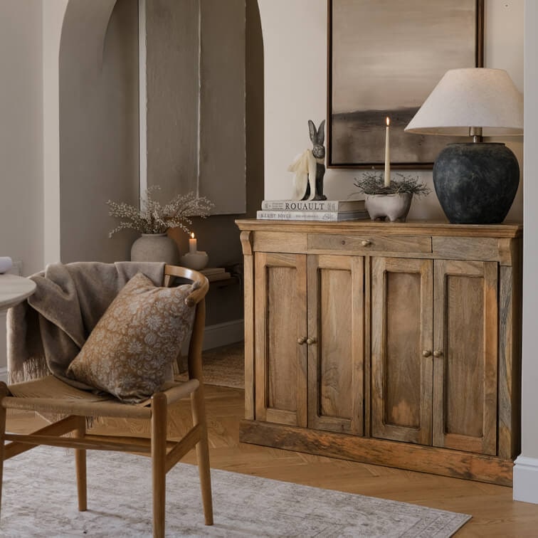 Aparador de madera en color natural con lámpara y decoración en salón acogedor con silla y cojín