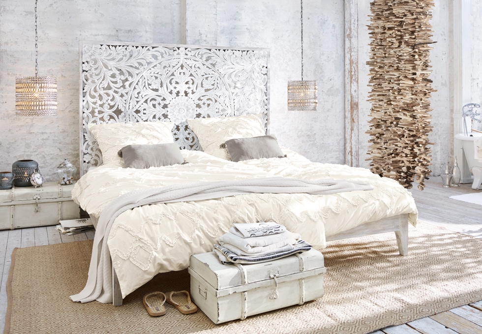 Dormitorio bohemio con cama blanca tallada, ropa de cama crema y decoración natural de madera y ratán