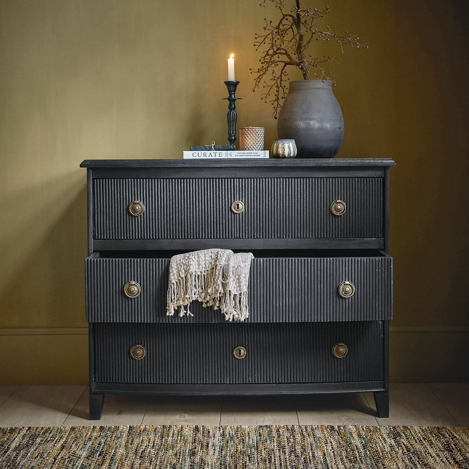 Cómoda Boissiére Cómoda negra de madera con tres cajones y manta decorativa beige, estilo vintage