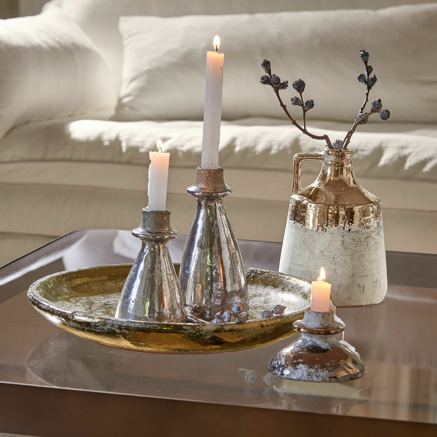Bandeja con jarrones Tameena Conjunto decorativo de candelabros y jarrón de cerámica en tonos plateados y dorados sobre mesa de cristal