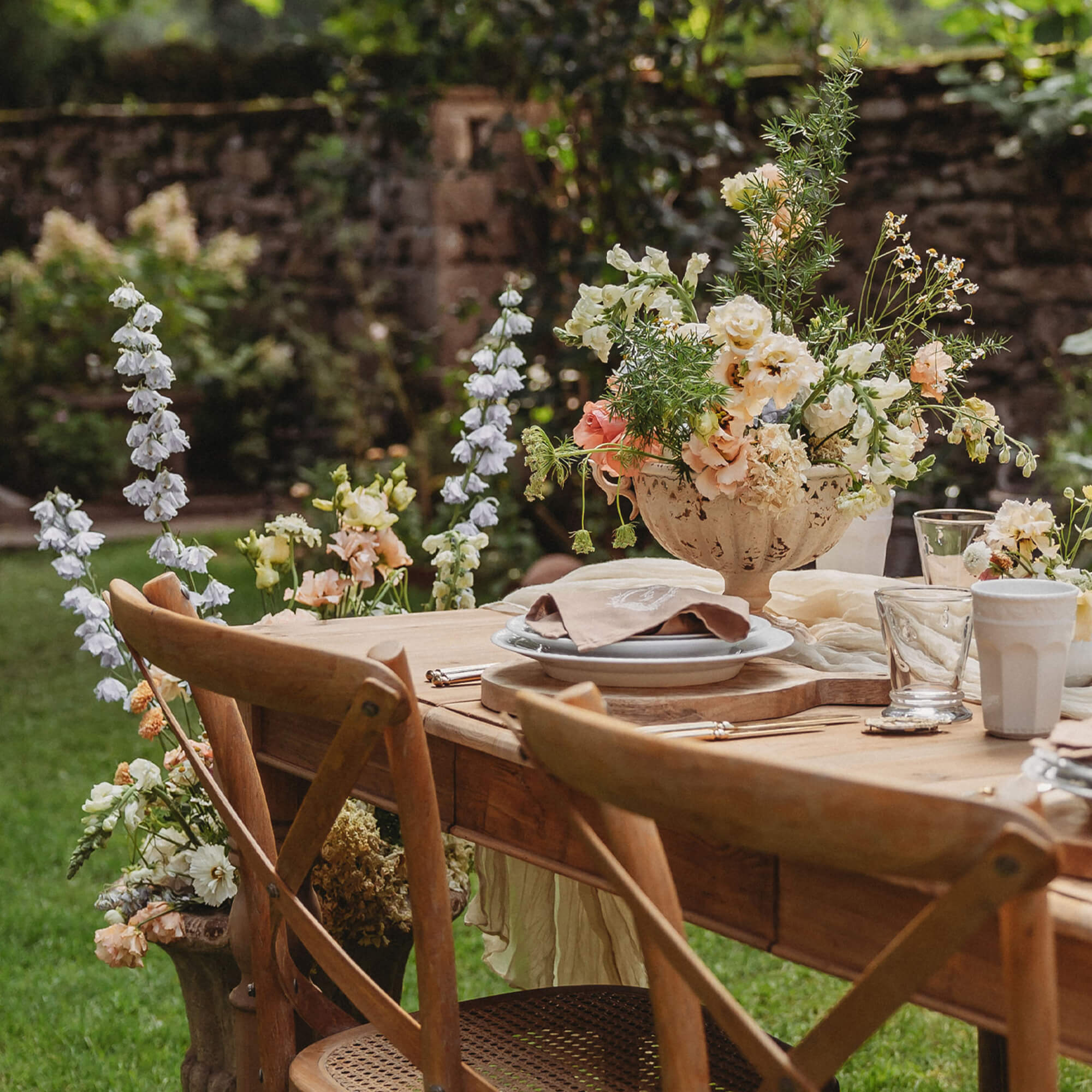 Mesa de jardín de madera con decoración floral y sillas naturales sobre césped verde