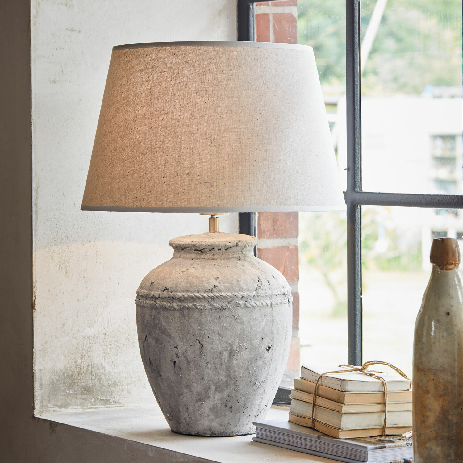 Lámpara de mesa Mosnay Lámpara de mesa de cerámica gris con pantalla beige sobre el alféizar junto a libros