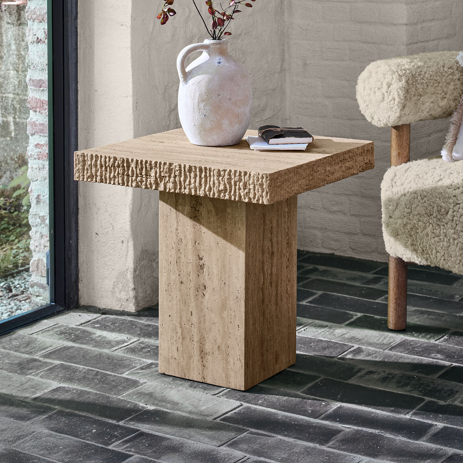 Mesa auxiliar cuadrada de travertino beige con jarra decorativa y libros encima