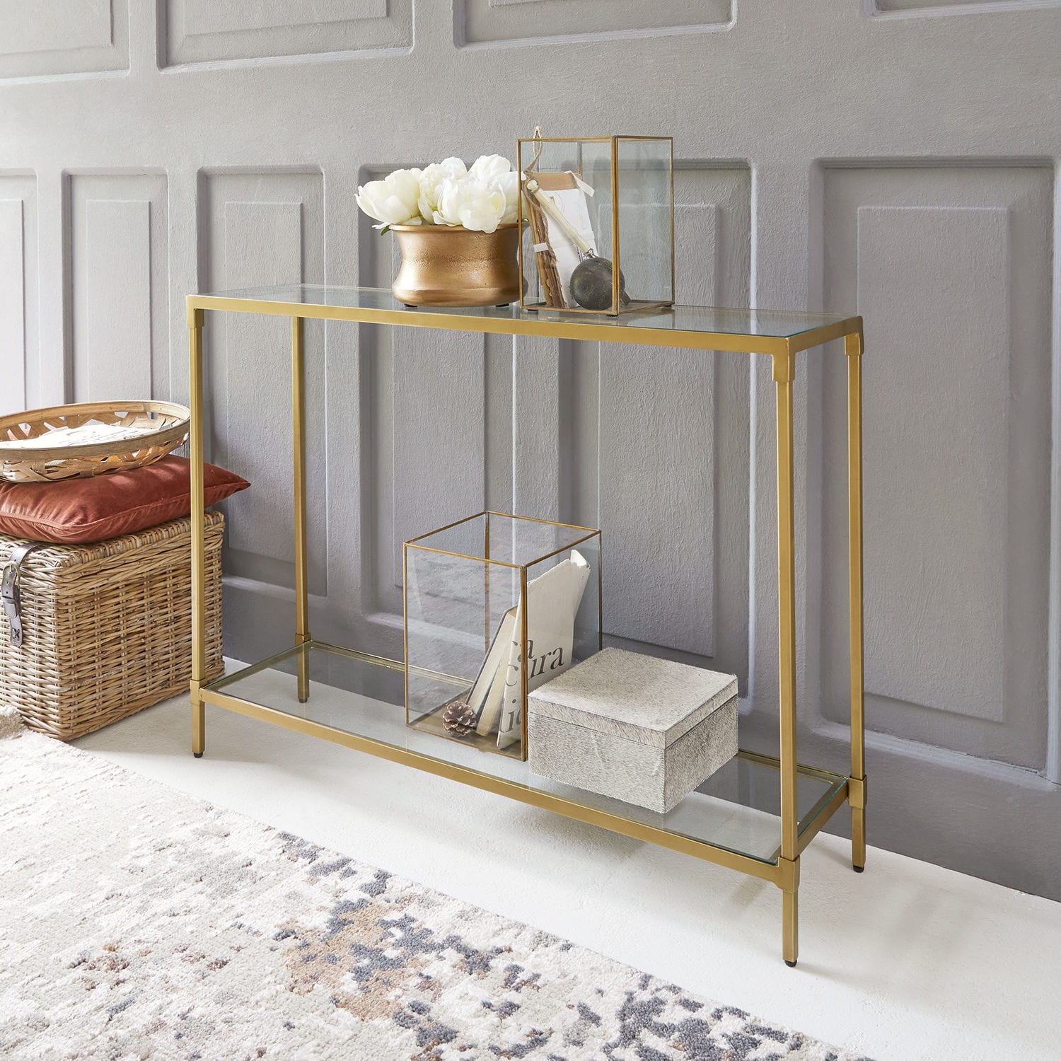 Consola Ninove Consola de vidrio con marco metálico dorado, decoraciones y cesta de mimbre en el suelo