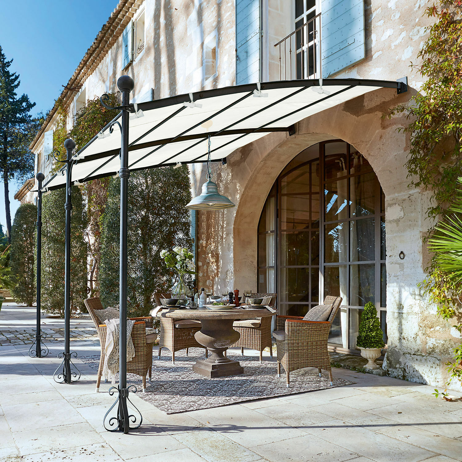 Pérgola Kattles Conjunto de muebles de jardín de mimbre bajo un toldo blanco en un patio de piedra frente a una casa de piedra