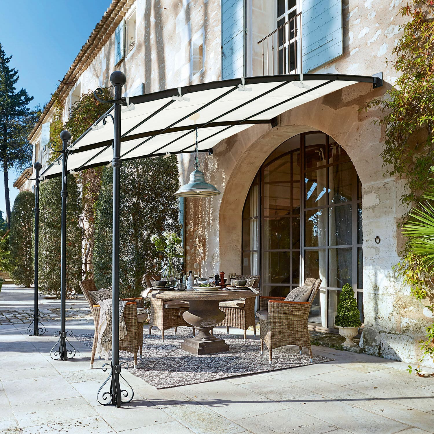 Pérgola Kattles Conjunto de muebles de jardín de mimbre bajo un toldo blanco en un patio de piedra frente a una casa de piedra