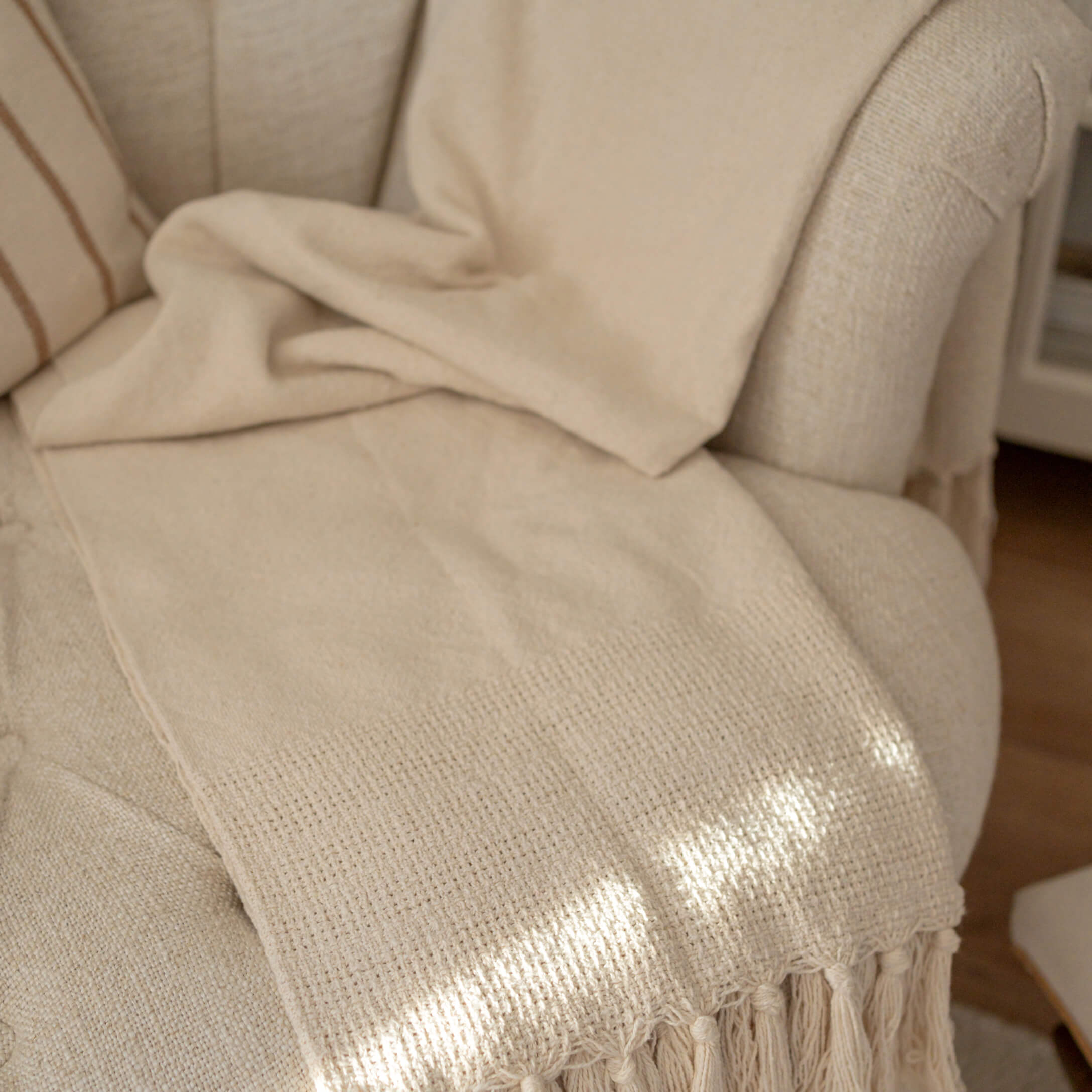 Manta beige con flecos sobre sillón claro, tejido suave para decoración y confort