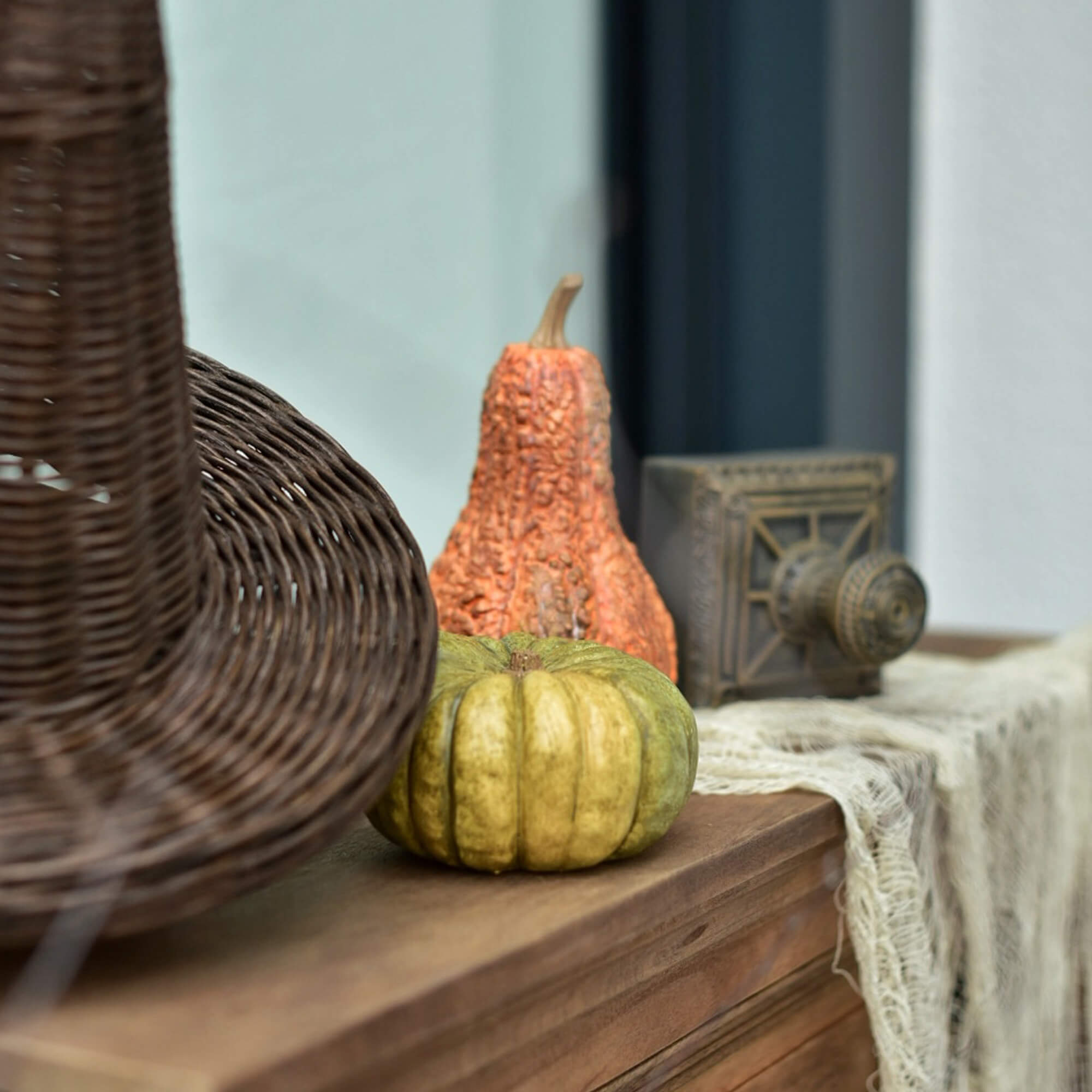 Calabazas decorativas verdes y naranjas sobre una superficie de madera junto a una cesta de mimbre