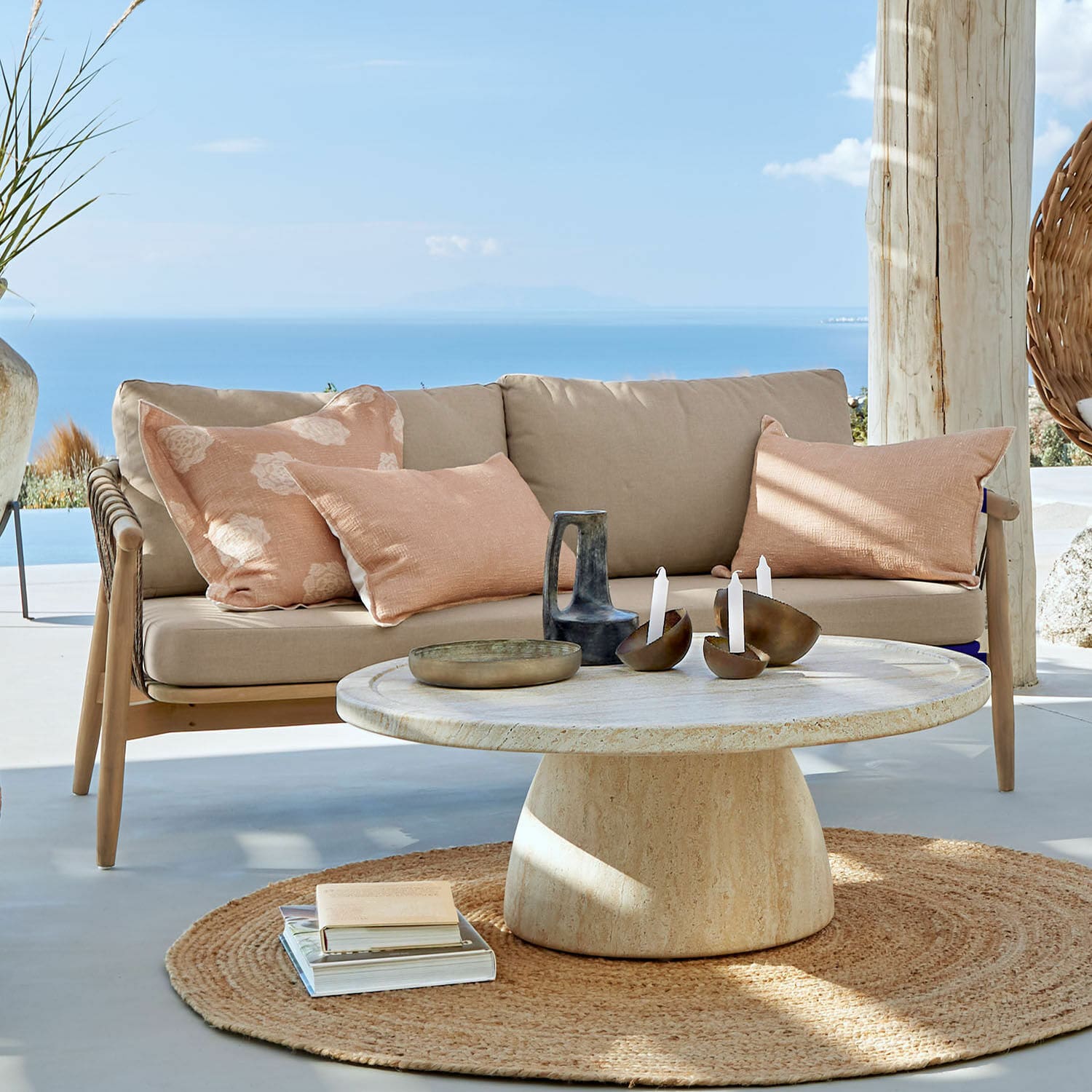 Sofá FSC®-100% Thornwick Sofá beige con cojines y mesa redonda de piedra en terraza con vista al mar